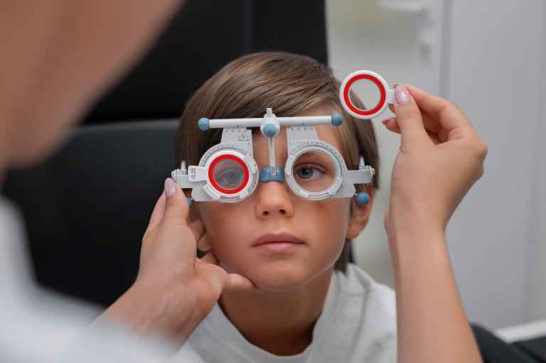 Child having comprehensive eye examination with phoropter testing device